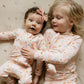 baby girl and toddler girl wearing matching baby bamboo pajama and toddler bamboo pajama set in pink with daisies and smiley faces