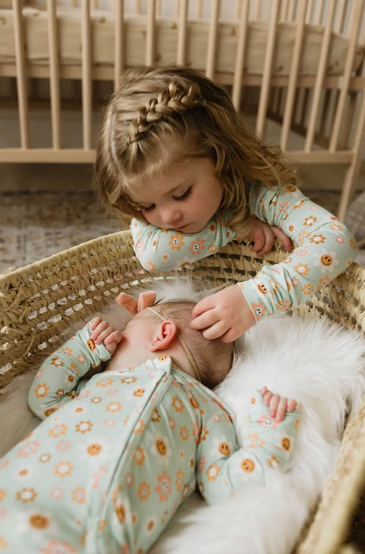 baby girl and toddler girl wearing matching aqua toddler bamboo pajama set and baby bamboo pajama set with daisies and smiley face print